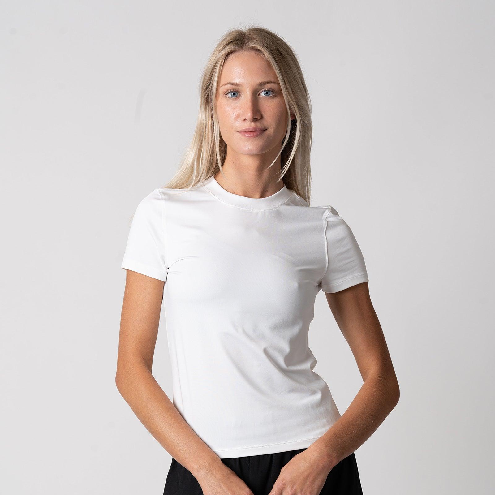 Frau trägt schlichtes weißes, kurzärmeliges T-Shirt vor weißem Hintergrund.