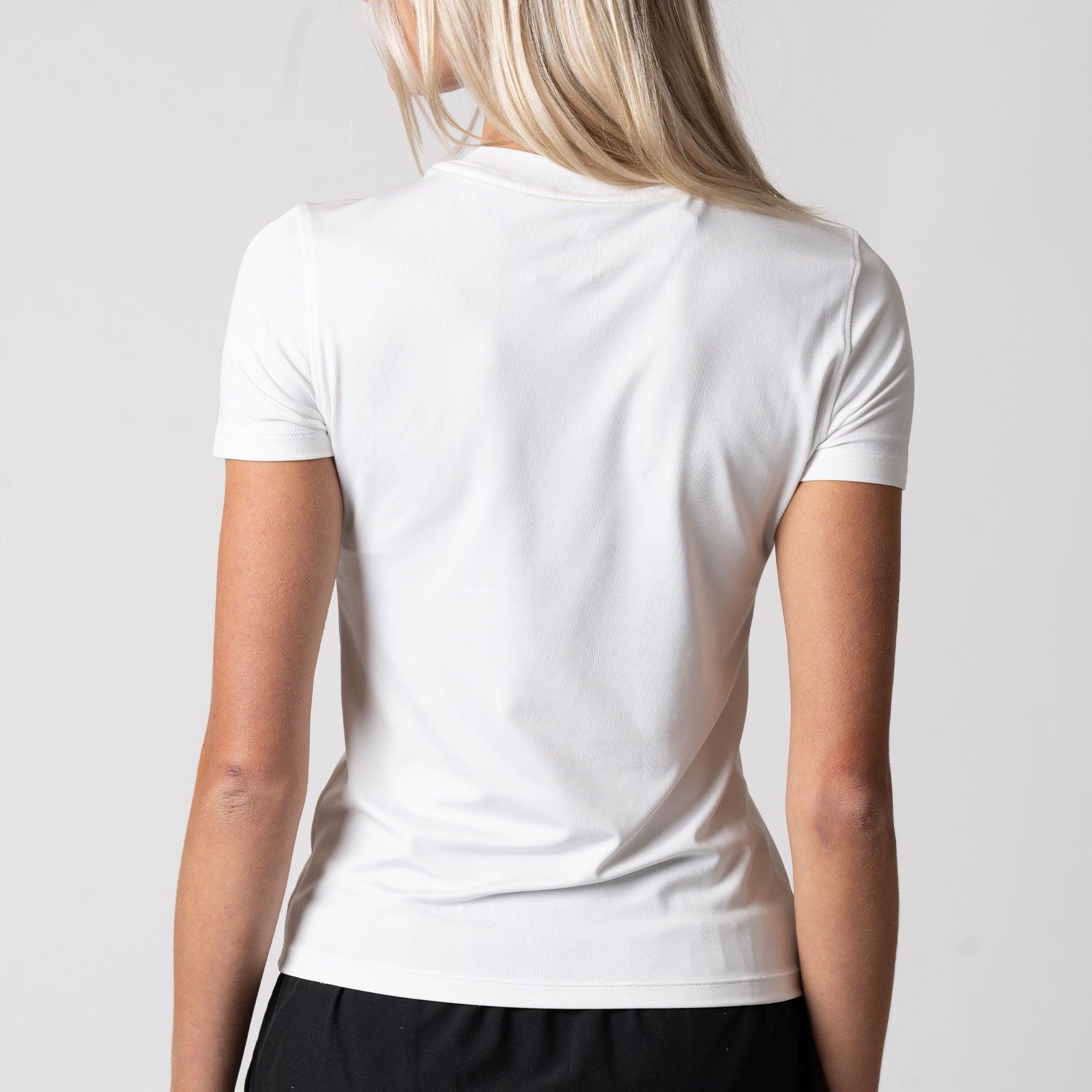 Frau von hinten trägt weißes, kurzärmeliges T-Shirt und schwarze Hose vor hellem Hintergrund.