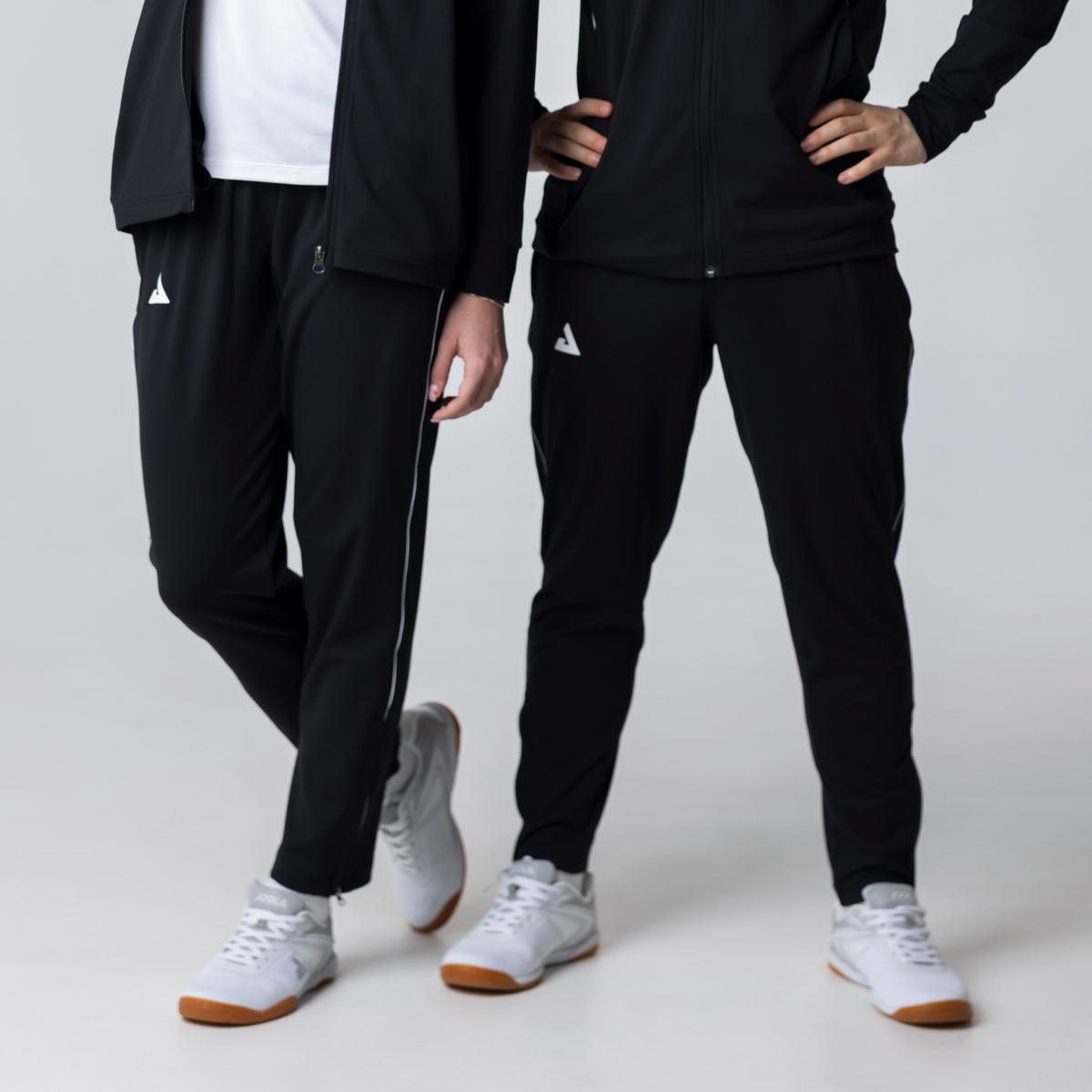 Zwei Personen tragen schwarze Sporthosen mit weißem Logo und weißen Sportschuhen vor hellem Hintergrund.