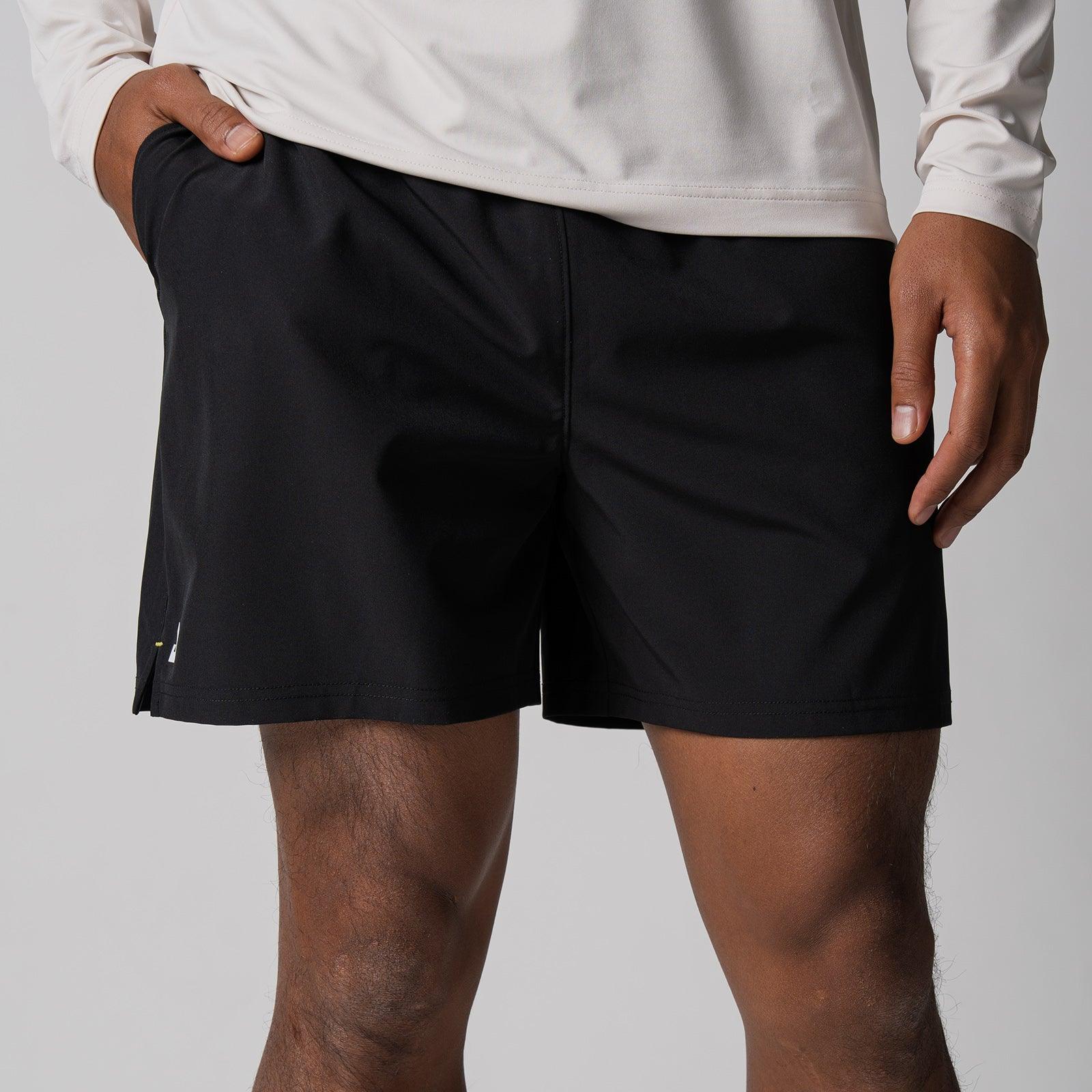 Schwarze kurze Sporthose aus leichtem Material, getragen von einem Mann mit weißem Langarmshirt.