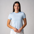 Frau trägt hellblaues, kurzärmeliges T-Shirt vor hellem Hintergrund.