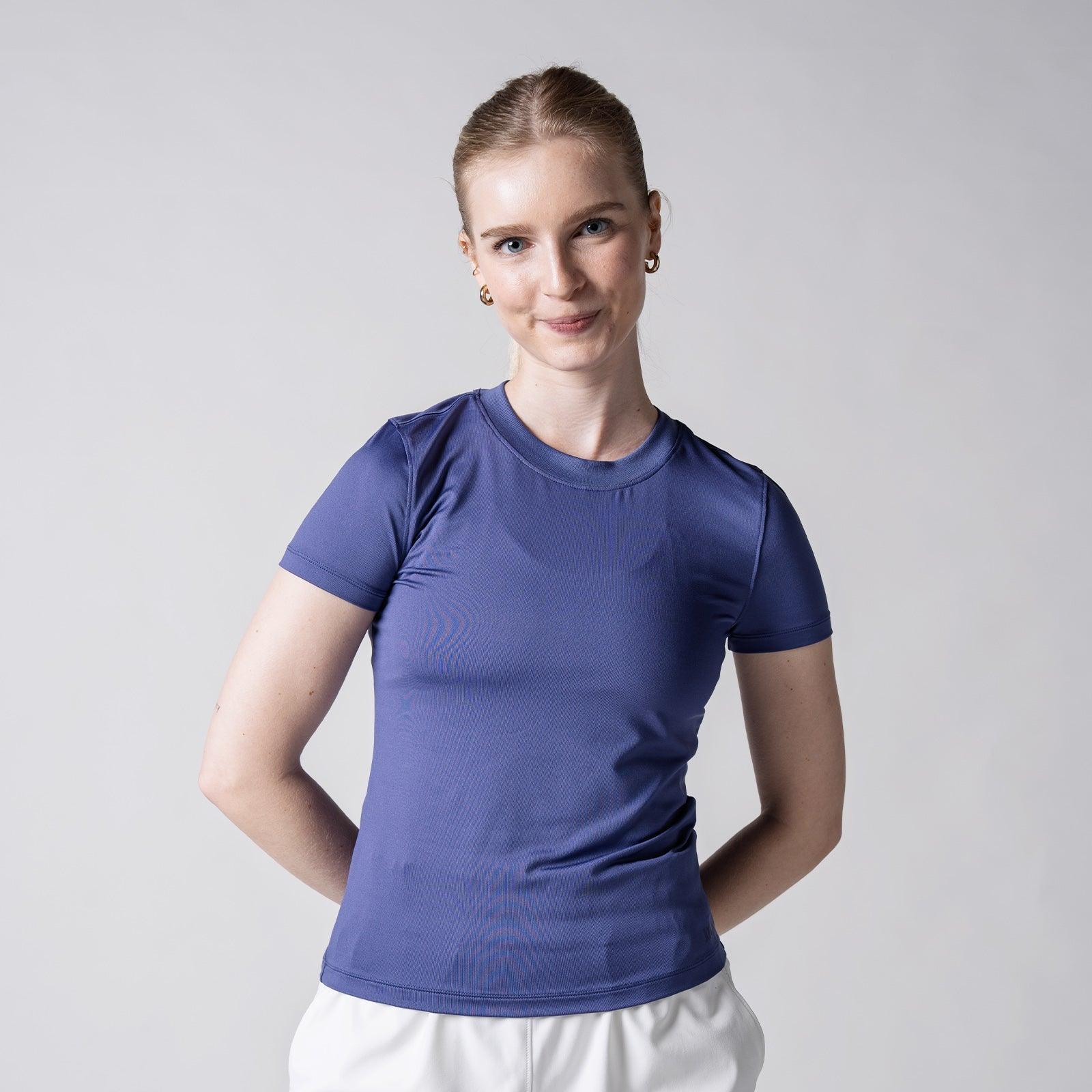 Frau trägt eng anliegendes, kurzes, violettes T-Shirt vor hellem Hintergrund.
