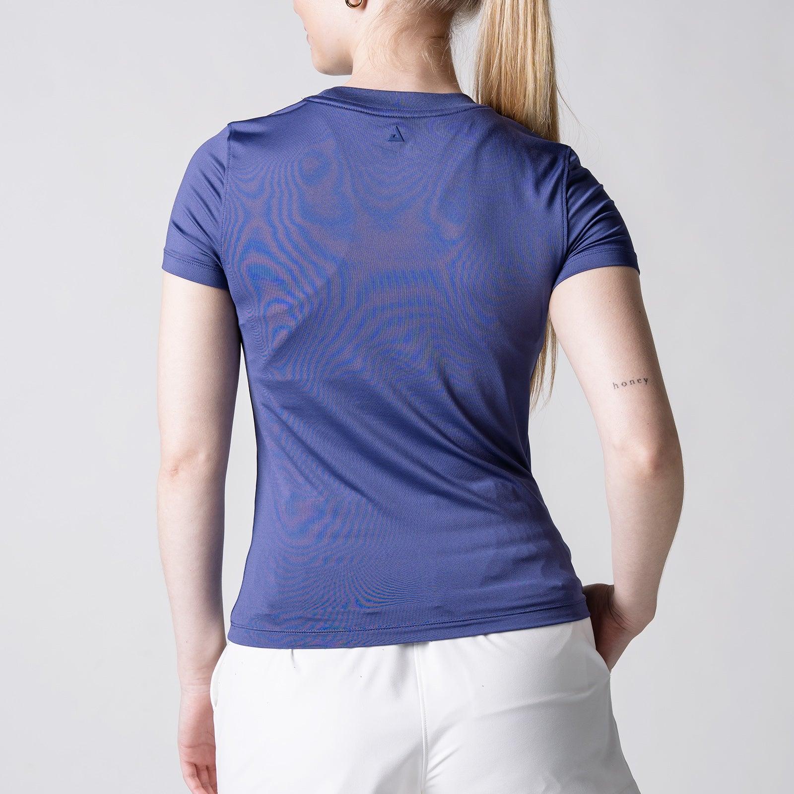 Frau von hinten in blauem, kurzärmligem Sportshirt und weißer Hose vor weißem Hintergrund.