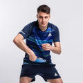 Junger Mann in blauem JOOLA Tischtennis-Outfit hält Tischtennisschläger in Spielposition.