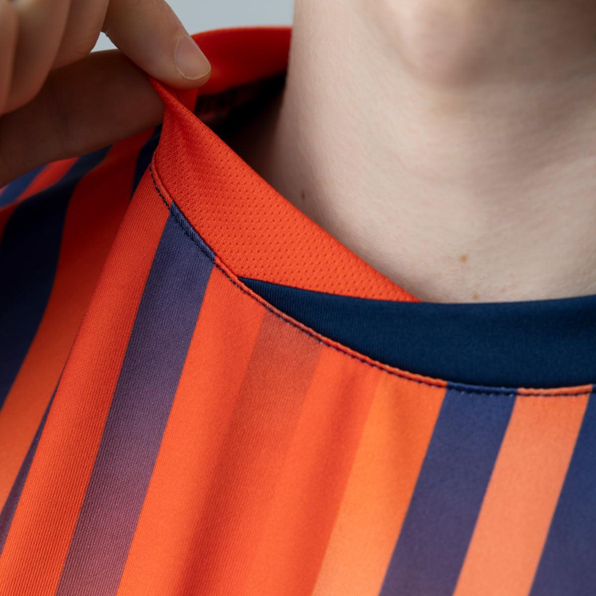Nahaufnahme eines rot-blau gestreiften Sporttrikots mit rundem Kragen, das von einer Hand leicht angehoben wird.
