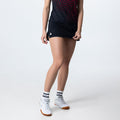 Frau trägt schwarzen Sportrock mit weißem Logo, weiße Sportsocken und weiße Sportschuhe, Vorderansicht, vor weißem Hintergrund.
