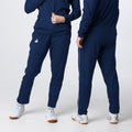 Dunkelblaue Sporthose mit weißem Seitenstreifen, vorne und hinten getragen, kombiniert mit weißen Sportschuhen.